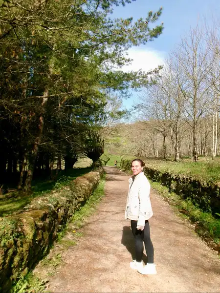 Agus caminando entre árboles y muros de piedra